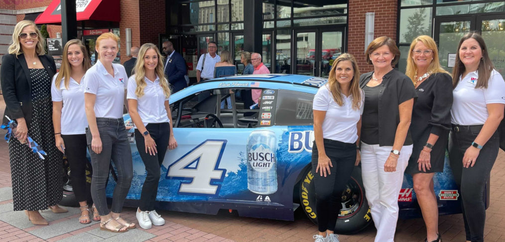 The Common Ground PR team stands in front of a blue NASCAR car